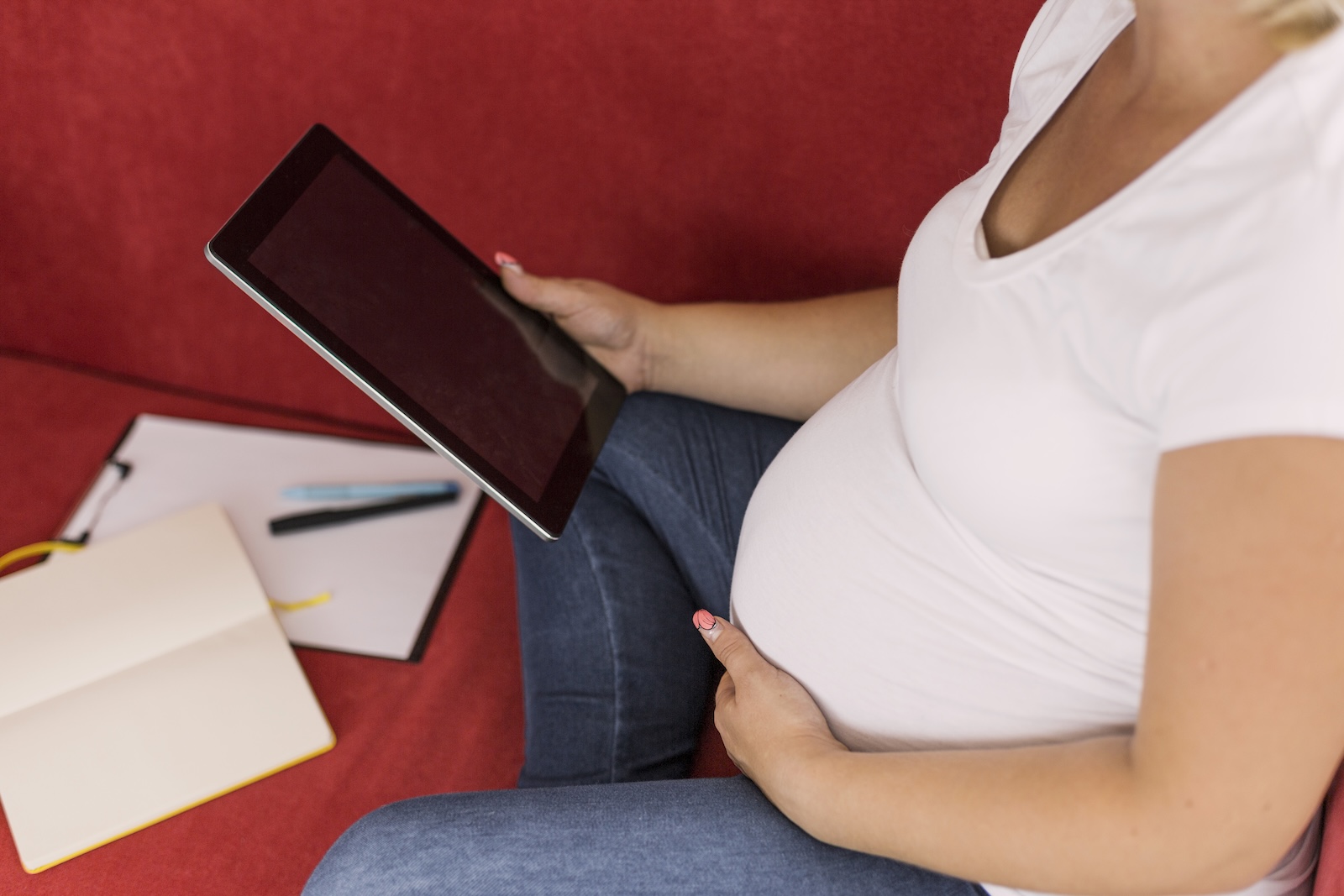 Pregnant woman comparing newborn stem cell banking options on a tablet, with a notebook and pen beside her