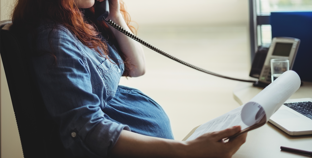 Pregnant woman on the phone reading a printed document while comparing cord blood banks